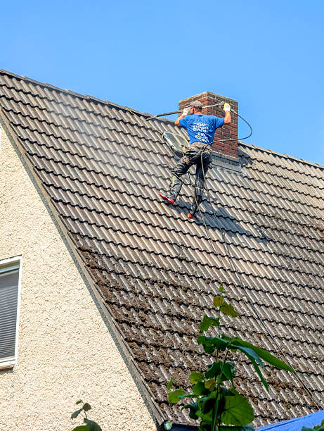 Worker performing roof cleaning with a high pressure washer on a residential building